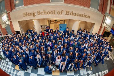 The Class of 2024 stands under the Neag School of Education sign in the atrium of the Gentry Building.
